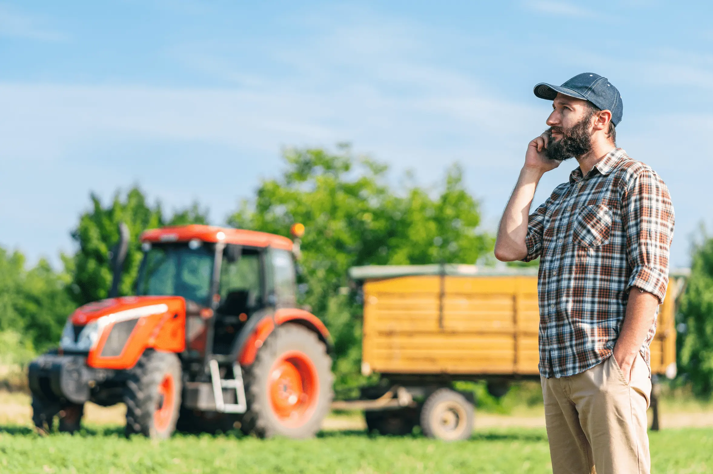 Vīrietis stāv pie traktora un runā pa telefonu